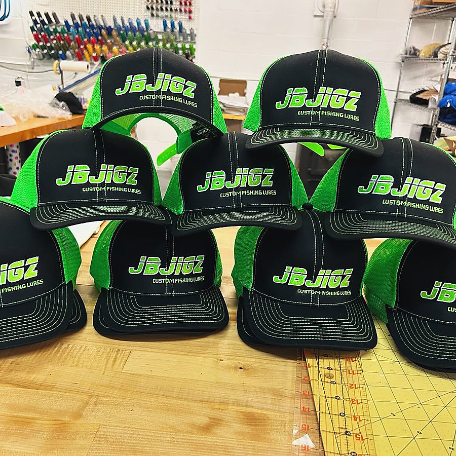 A stack of black and neon green JB Jigz caps on the workroom bench