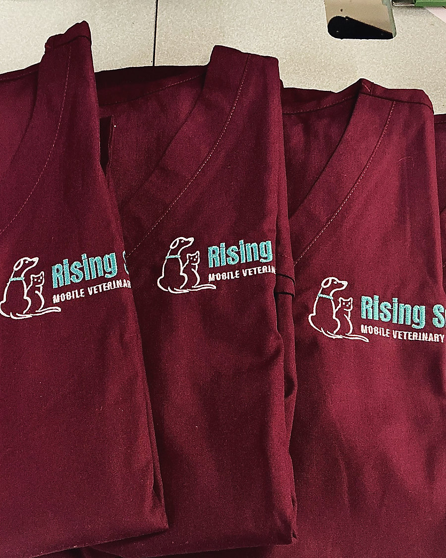 Maroon scrub tops embroidered with a mobile veterinary logo: a dog and a cat in white