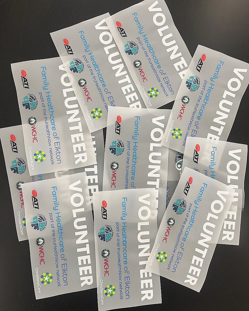 A pile of printed direct-to-film transfers reading Volunteer, each with a row of sponsor logos
