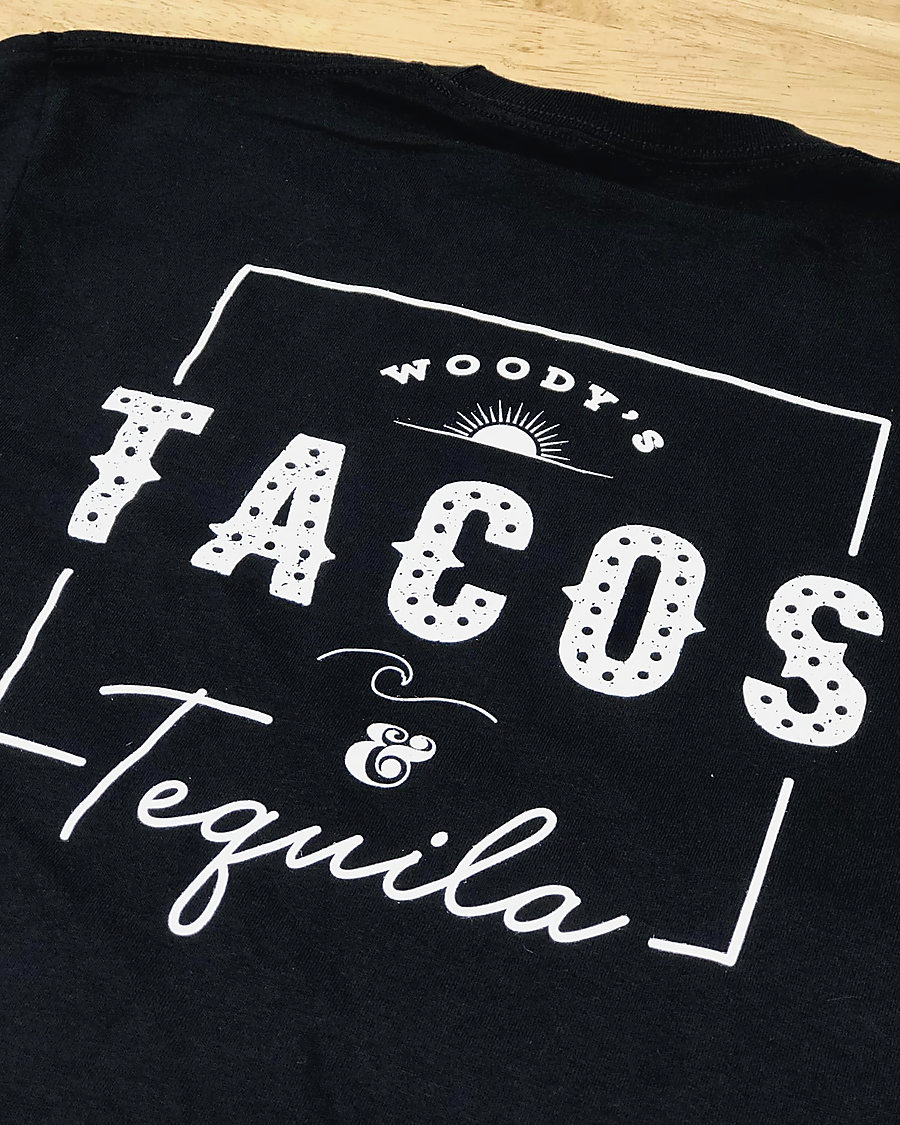 The back of a black T-shirt screen printed in white: Woody’s Tacos and Tequila